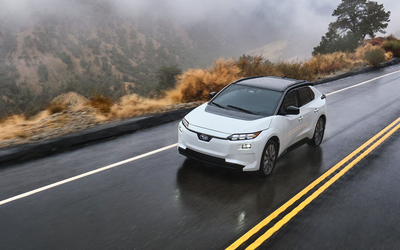 A Solterra AWD electric SUV drives on a narrow mountain road in the rain.