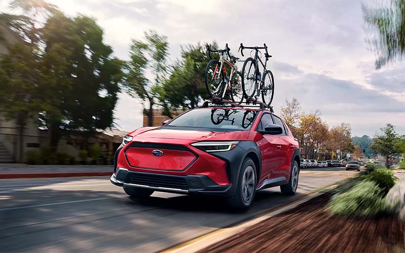2024 Subaru Solterra driving in the city with a bike rack on top of car